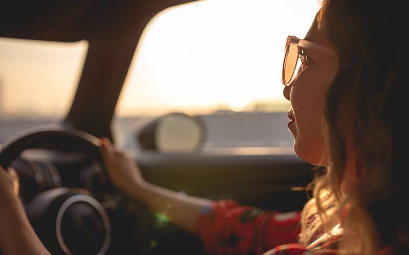 Smart driver wearing sunglasses driving an electric car at sunset.